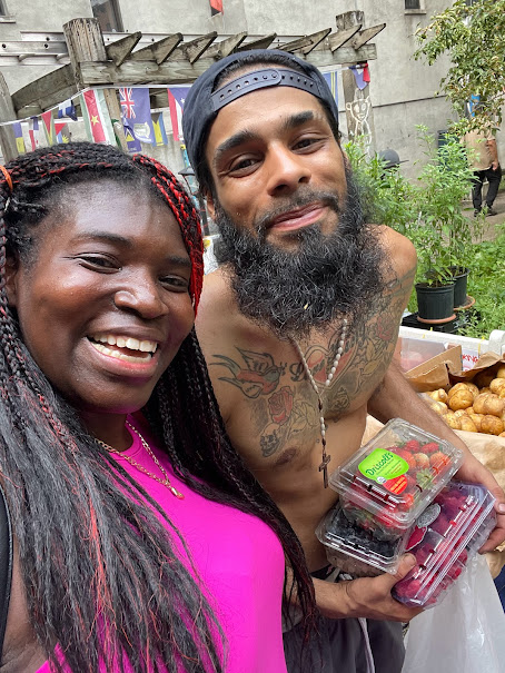 Two smiling community members holding fresh fruit during a neighborhood support event